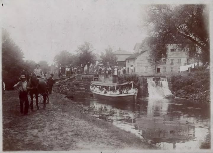 Historic photograph of a canal boat at a lock, with people and a horse on the bank